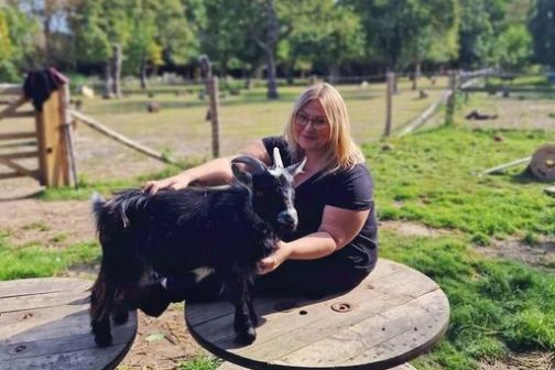 Woman sitting outdoors petting a goat on wooden spools.