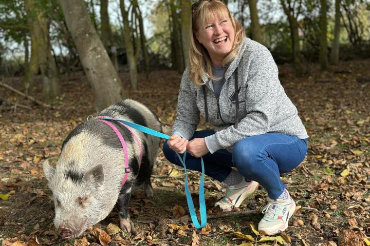 Woman squatting in woods, smiling, holding a leashed pig.