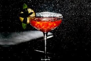 Red cocktail in a glass with lime garnish, against a dark, misty background.